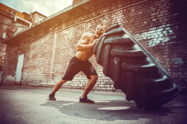 Muskulöse Fitness hemdloser Mann bewegt großen Reifen. — Stockfoto