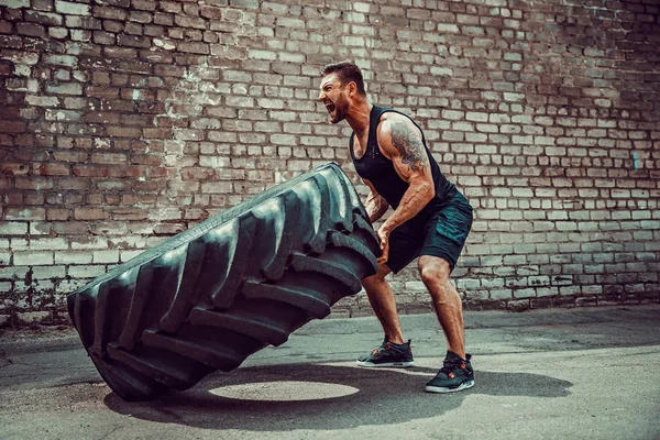 Muskulöser Fitness-Mann bewegt großen Reifen. — Stockfoto
