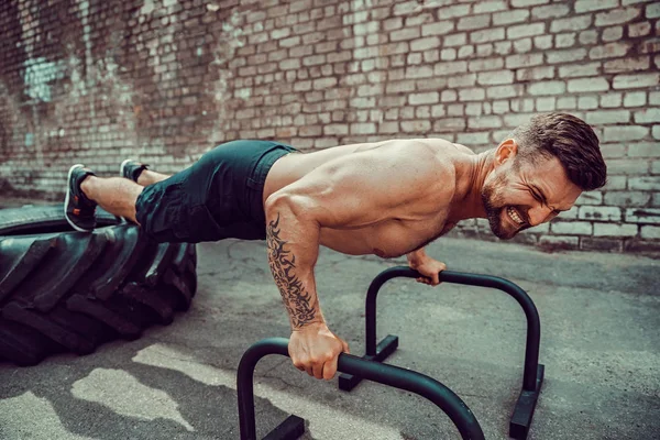 Strong sporty happy cheerful positive man doing press exercises holding plank outdoors — Stock Photo, Image