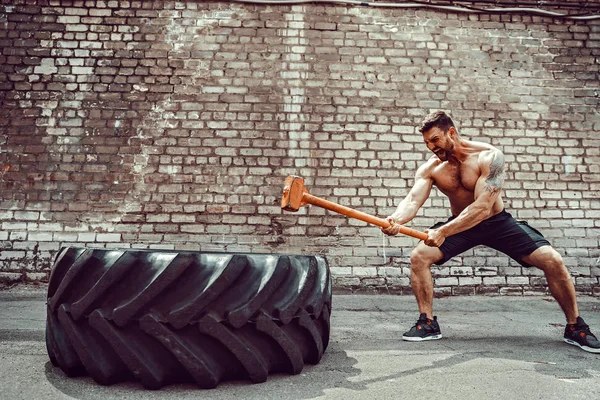 Sport Fitness Man Hitting Wheel Tire With Hammer Sledge Cross fit Training.