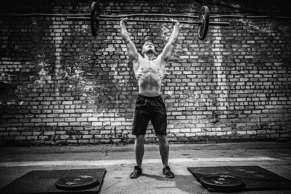 Un uomo muscoloso che fa ginnastica all'aperto con un bilanciere in testa. Formazione funzionale . — Foto Stock