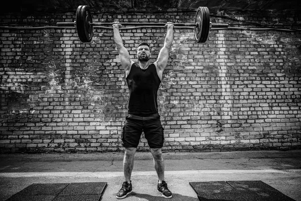 Gespierde fitness man doen deadlift een barbell boven zijn hoofd in outdoor, straat sportschool. Functionele training. — Stockfoto