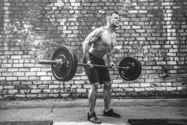 Atletik bir adam bir halter ile çalışma dışarı. Güç ve motivasyon. Arka kasları için egzersiz