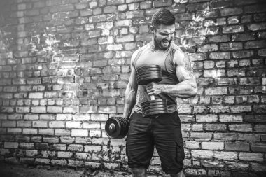 kaslı adam bir tuğla duvara dumbbell ile yapıyor