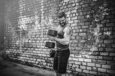 kaslı adam bir tuğla duvara dumbbell ile yapıyor
