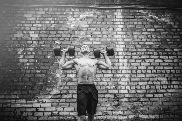 Izmos srác gyakorolja a súlyzó ellen egy téglafal — Stock Fotó