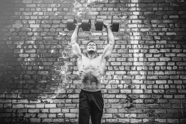 Musculoso chico haciendo ejercicios con mancuerna contra una pared de ladrillo — Foto de Stock