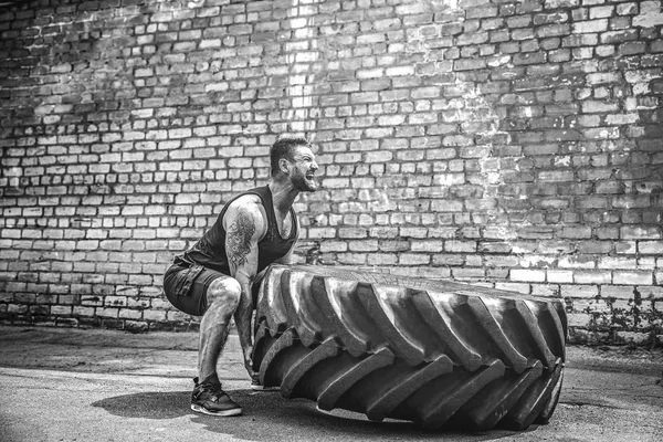 Muscular fitness shirtless man moving large tire.