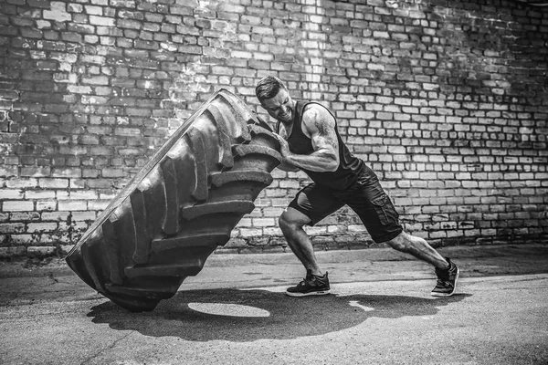 Muscular fitness shirtless man moving large tire.