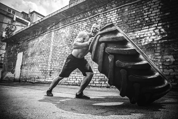Muskulöse Fitness hemdloser Mann bewegt großen Reifen. — Stockfoto