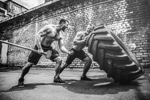 Két izmos sportolók képzés. Izmos fitness félmeztelen férfi mozgó nagy gumiabroncs — Stock Fotó