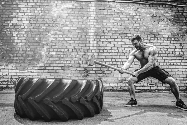 Sport-Fitness-Mann schlägt mit Hammer Rodel Crossfit-Training auf Radreifen auf. — Stockfoto