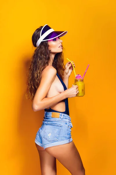 Seksi kadın trendy güneşlik içecek holding beyaz mayo ve kot şort, — Stok fotoğraf
