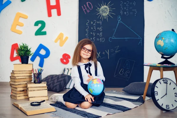 Portrait d'une belle jeune écolière tenant globe assis sur le tapis . — Photo