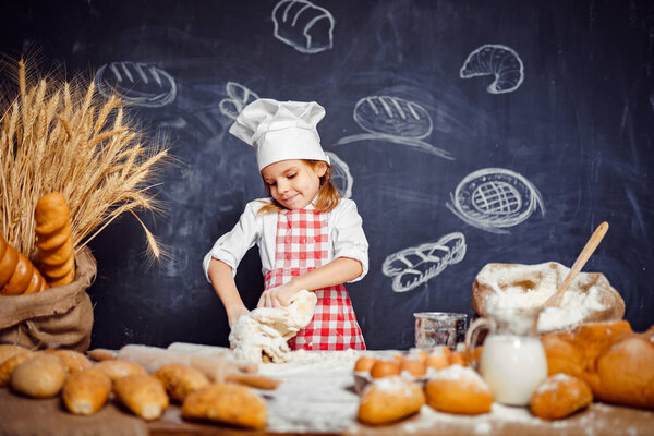 Милая маленькая девочка в шляпе шеф-повара делает тесто
