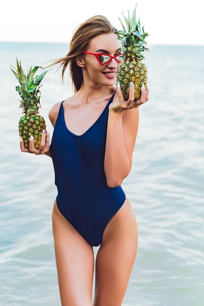 Девушка-модель в монокини на морском берегу тропического острова с двумя ананасами — стоковое фото