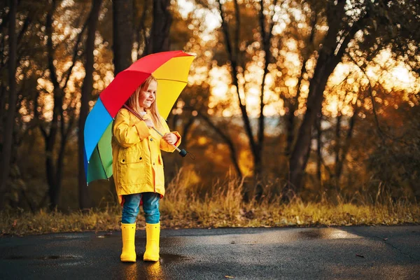 Funny cute toddler girl wearing waterproof coat with colorful umbrella playing in the garden by rainy and sunny day