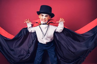 Cadılar Bayramı vampir çocuk kırmızı studio arka plan üzerinde çevrili elleri ile siyah, kırmızı pelerinini dalgalar.