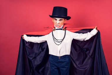 Cadılar Bayramı vampir çocuk kırmızı studio arka plan üzerinde çevrili elleri ile siyah, kırmızı pelerinini dalgalar.