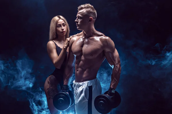 Attraktivt par, en smal blond kvinnlig och stilig bar överkropp kille poserar på studio på en mörk texturerat bakgrund. — Stockfoto