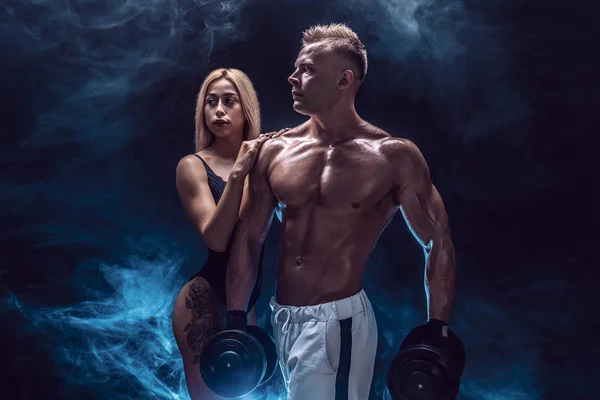 Attractive couple, a slim blonde female and handsome shirtless guy posing at studio on a dark textured background. — Stock Photo, Image