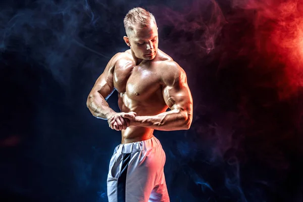 Guapo fuerte culturista posando en estudio sobre humo fondo — Foto de Stock