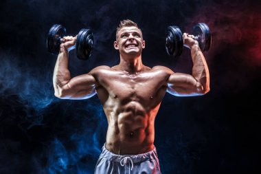 Konsantre olmuş kaslı adam dambılla egzersiz yapıyor.