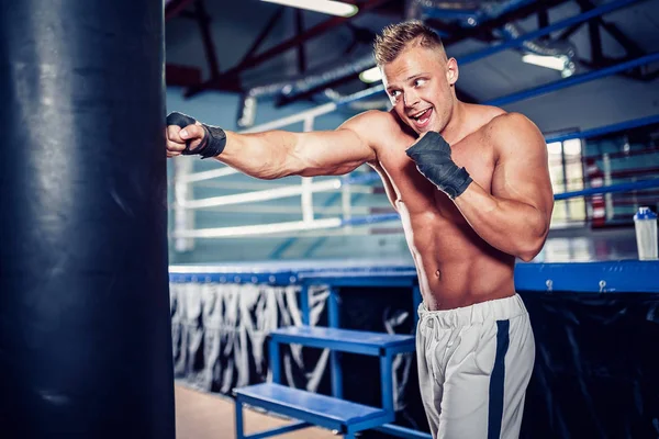 Тренування чоловіка боксера з мішком для ударів у темному спортивному залі . — стокове фото