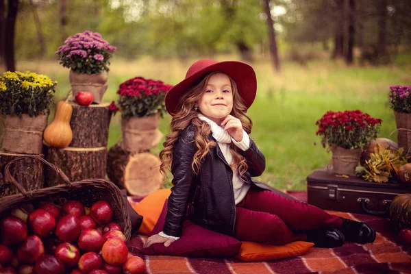 Criança sorridente com cesta de maçãs vermelhas sentadas no parque de outono — Fotografia de Stock