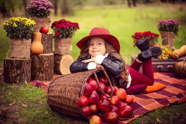 Улыбающийся ребенок с корзиной красных яблок сидит в осеннем парке — стоковое фото