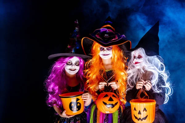 Tres Hermosa chica en un disfraz de bruja sobre un fondo oscuro en humo asustando y haciendo caras — Foto de Stock