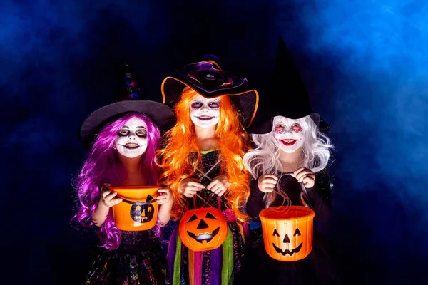 Drei schöne Mädchen in einem Hexenkostüm vor dunklem Hintergrund in Rauch, der Angst macht und Gesichter macht — Stockfoto