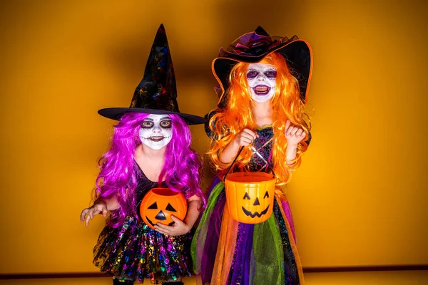 Dos Hermosa chica en un disfraz de bruja sobre un fondo amarillo asustando y haciendo caras — Foto de Stock