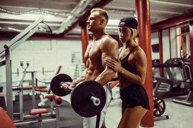 Genç bir adam ve bir kadın takımı dambıllarla antrenman yapıyor.