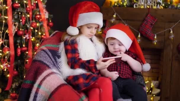 Two children in Christmas decorations playing smartphone — Stock Video