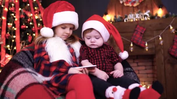 Two children in Christmas decorations playing smartphone — Stock Video