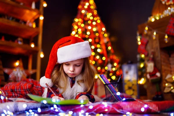 Grappig meisje in Kerstman hoed schrijft een brief aan de Kerstman — Stockfoto