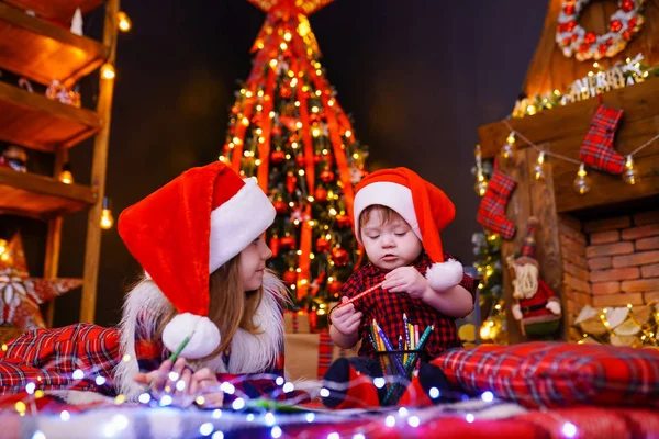 Funny girl in Santa hat écrit une lettre au Père Noël et à son frère liitle — Photo