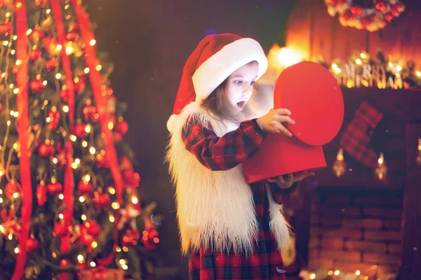 Adorable petite fille ouvrant un cadeau de Noël magique par un arbre de Noël dans le salon confortable en hiver — Photo