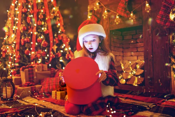 Adorable petite fille ouvrant un cadeau de Noël magique par un arbre de Noël dans le salon confortable en hiver — Photo