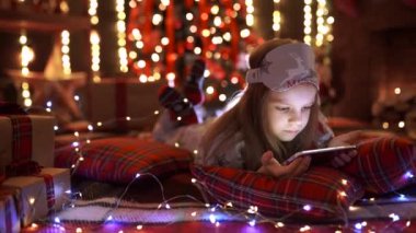 Kız pijama tablet, Noel ağacı ve şömine yakın dinlenme süre smartphone ile oynamak.
