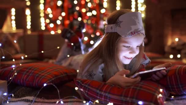 Κορίτσι παίζει με το tablet, το smartphone κοντά στο χριστουγεννιάτικο δέντρο — Αρχείο Βίντεο