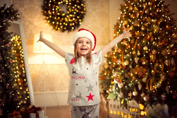 Glad glad tjej i jul pyjamas, santa helper hatt höjde händerna upp. — Stockfoto