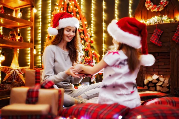 Весела мама та її мила донька обмінюються подарунками. Батьки і маленькі діти розважаються біля дерева в приміщенні. Любляча сім'я з подарунками в різдвяній кімнаті . — стокове фото