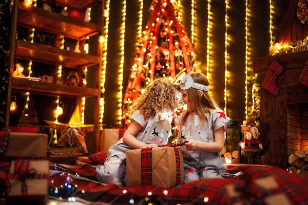 Szczęśliwy, że małe dziewczynki piżamie Boże Narodzenie otwiera pudełko przy kominku w salonie ciemny w Wigilię Bożego Narodzenia. — Zdjęcie stockowe