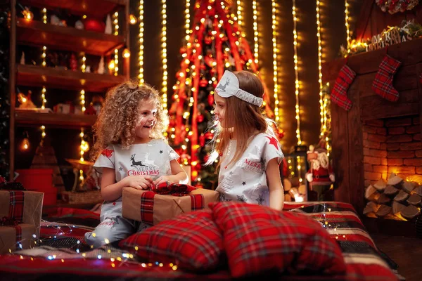 Jolies petites filles portant un pyjama de Noël boîte cadeau ouverte près d'une cheminée dans un salon sombre confortable la veille de Noël . — Photo