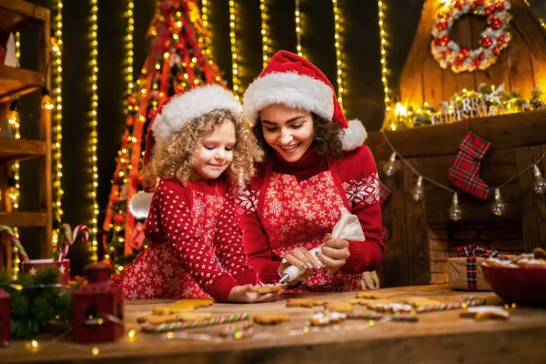 Щасливого Різдва і щасливих свят. Весела мила кучерява маленька дівчинка і її старша сестра в капелюхах Сантаса готують різдвяне печиво . — стокове фото