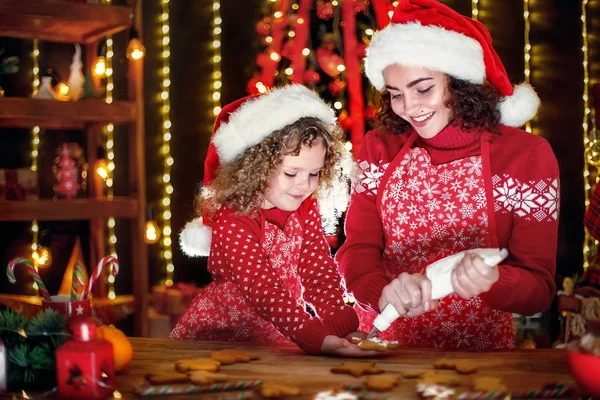 Merry Christmas and Happy Holidays. Cheerful cute curly little girl and her older sister in santas hats cooking Christmas cookies.