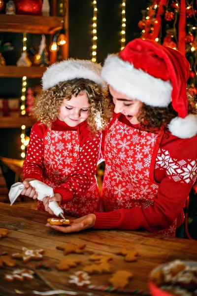 Wesołych Świąt i Wesołych Świąt. Wesoły ładny kręcone mała dziewczynka i jej starsza siostra w kapeluszach santas gotowania ciasteczka świąteczne. — Zdjęcie stockowe