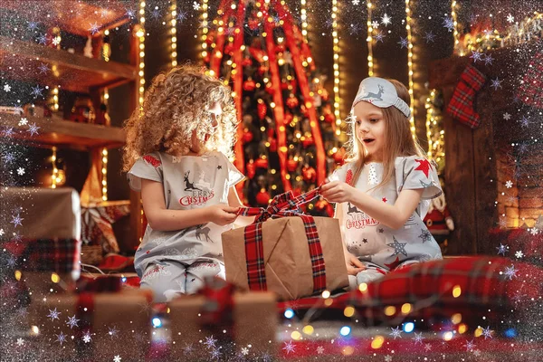Щасливі маленькі дівчата в різдвяній піжамі відкрили подарункову коробку біля каміна в затишній темній вітальні напередодні Різдва . — стокове фото